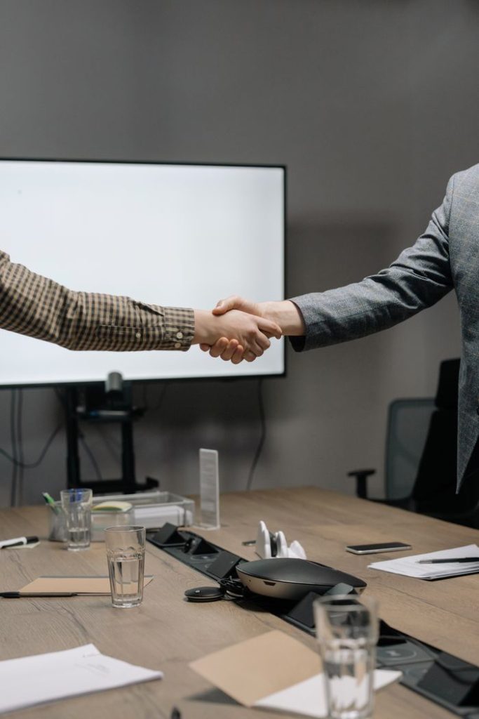 pexels photo 6814524 6814524 Two business professionals shaking hands in a modern meeting room, symbolizing successful collaboration.